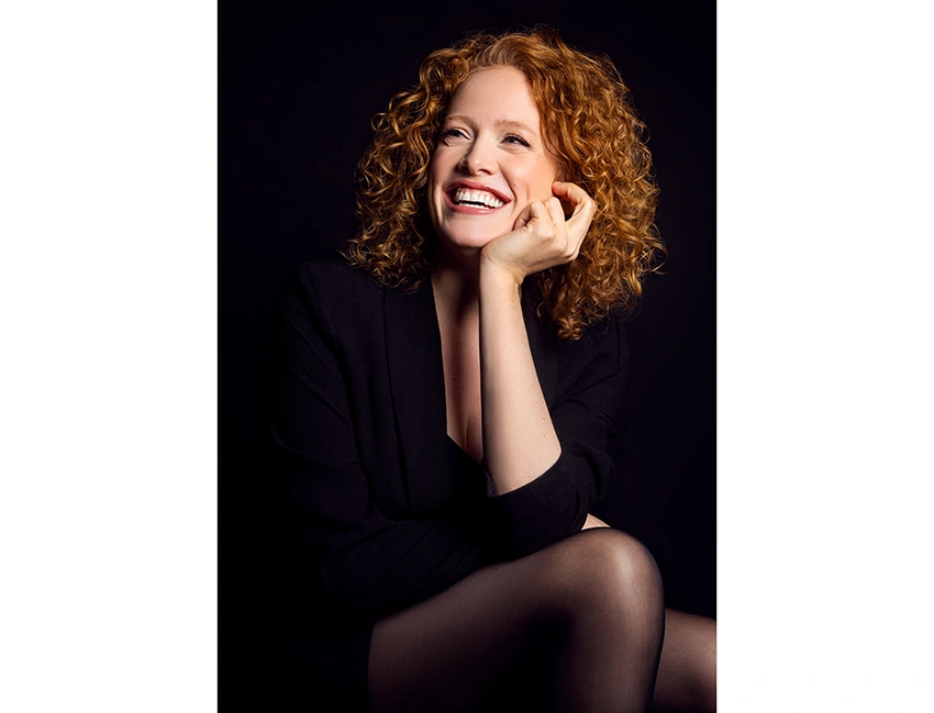 photo of a smiling redheaded person looking away from the camera against a dark background